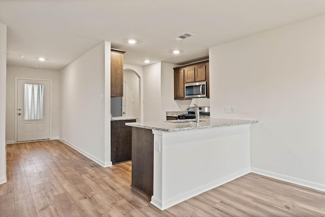 kitchen with a peninsula, stainless steel microwave, visible vents, and light stone countertops