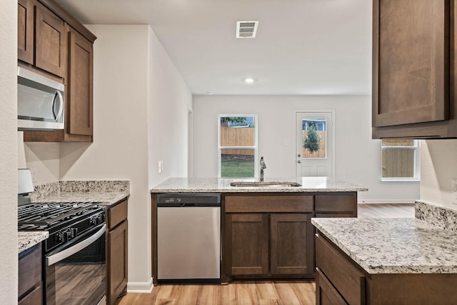 kitchen with stainless steel appliances, a sink, visible vents, light wood-style floors, and light stone countertops