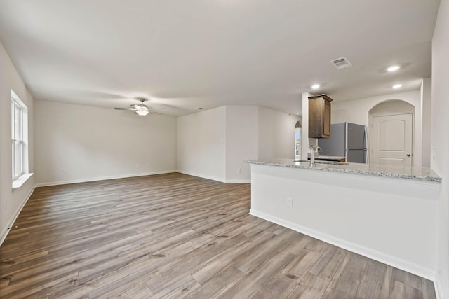 kitchen featuring light wood-style flooring, freestanding refrigerator, a sink, light stone countertops, and a peninsula