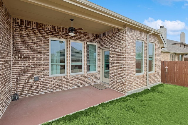 doorway to property featuring brick siding, a patio area, fence, and a ceiling fan