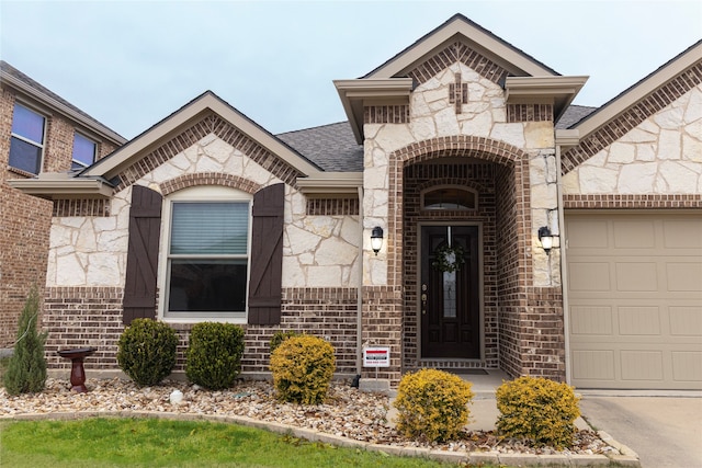 view of exterior entry with stone siding, brick siding, an attached garage, and a shingled roof