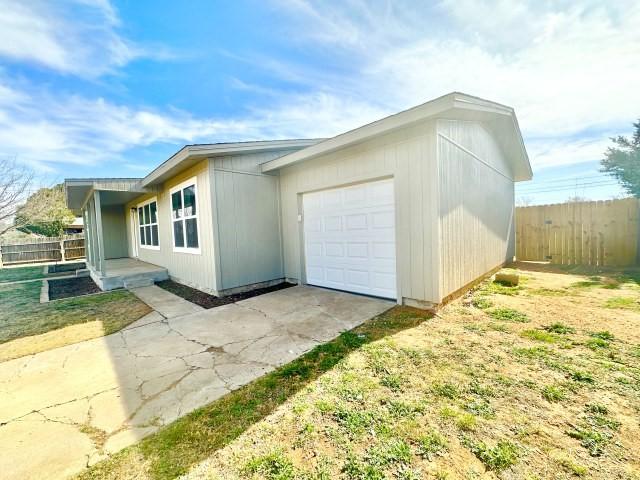 view of side of home featuring fence, driveway, an attached garage, and a lawn