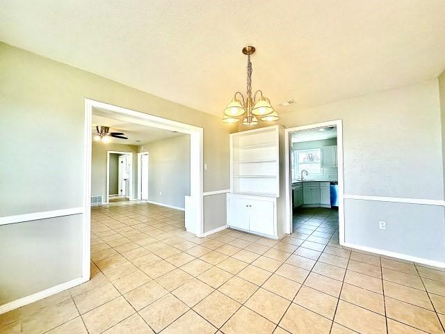 empty room with ceiling fan with notable chandelier, light tile patterned flooring, and baseboards