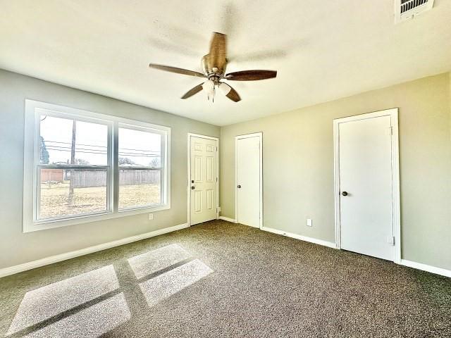 carpeted spare room featuring baseboards, visible vents, and ceiling fan