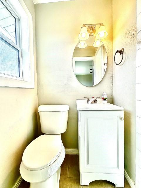 half bath with toilet, wood finished floors, vanity, and baseboards