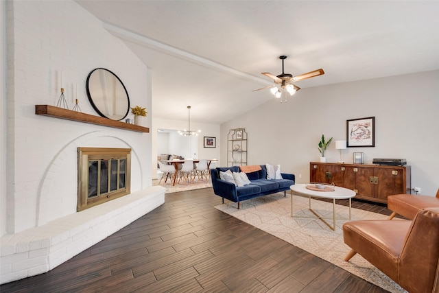 living room with a fireplace, vaulted ceiling, dark wood-type flooring, and ceiling fan with notable chandelier