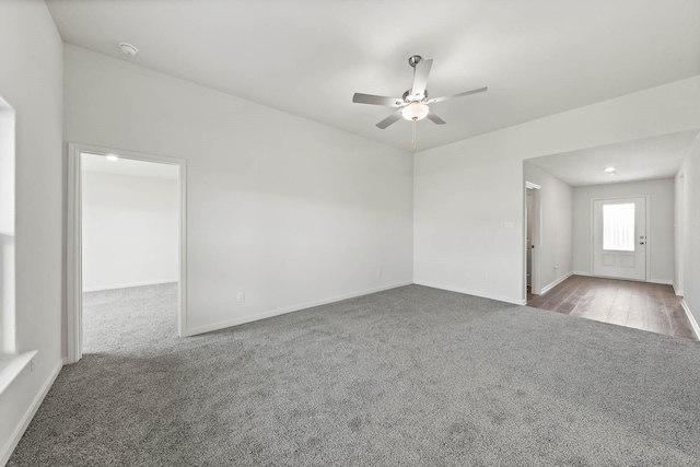 empty room featuring dark colored carpet, ceiling fan, and baseboards