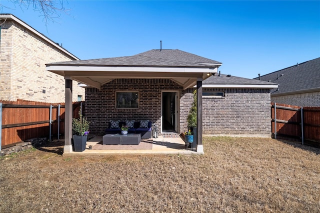 rear view of property featuring a patio, a fenced backyard, brick siding, a shingled roof, and an outdoor living space