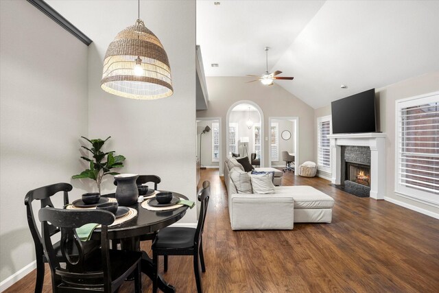 dining room with arched walkways, dark wood-type flooring, a ceiling fan, baseboards, and a lit fireplace