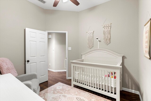 bedroom featuring a nursery area, a ceiling fan, baseboards, and dark wood-style flooring