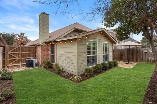 back of property featuring brick siding, a yard, a chimney, central AC, and fence