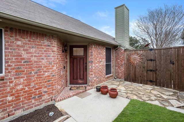 property entrance with brick siding, a patio, a chimney, roof with shingles, and a gate