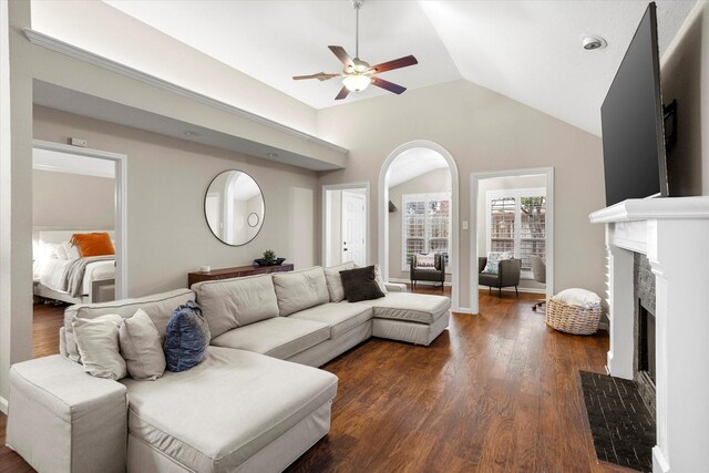 living area featuring dark wood-type flooring, arched walkways, vaulted ceiling, and a premium fireplace