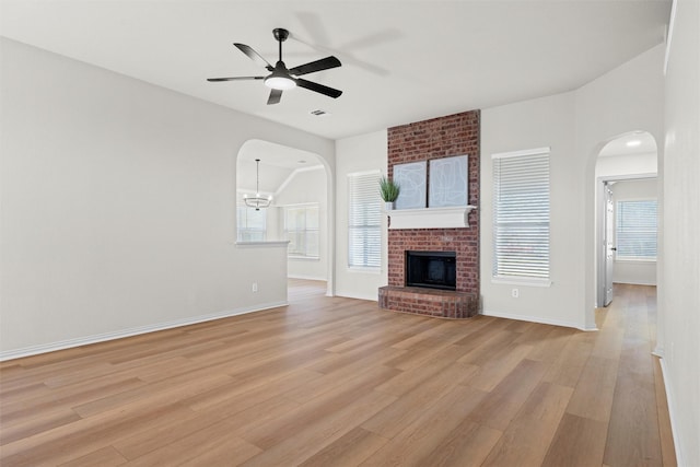 unfurnished living room featuring light wood finished floors, a fireplace, a wealth of natural light, and ceiling fan with notable chandelier