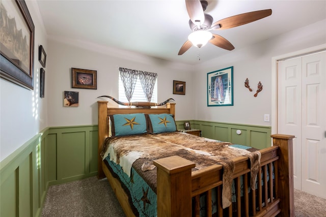 bedroom featuring ceiling fan, a decorative wall, carpet flooring, a closet, and wainscoting