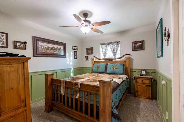 bedroom featuring a wainscoted wall, ceiling fan, and dark colored carpet