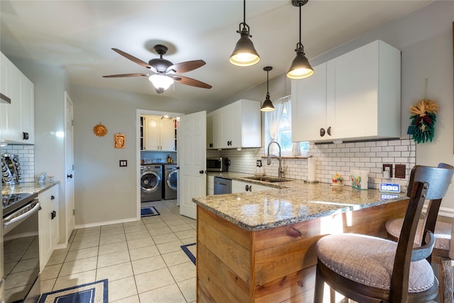 kitchen with stainless steel appliances, washing machine and dryer, white cabinetry, a sink, and light stone countertops