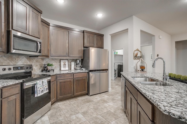 kitchen with light tile patterned flooring, light stone counters, a sink, stainless steel appliances, and decorative backsplash