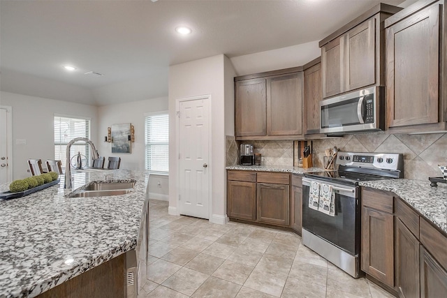 kitchen with a sink, decorative backsplash, appliances with stainless steel finishes, and light stone countertops