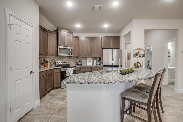kitchen with visible vents, a breakfast bar area, tasteful backsplash, a sink, and appliances with stainless steel finishes