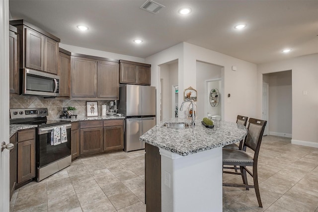 kitchen featuring light stone countertops, appliances with stainless steel finishes, a sink, a breakfast bar area, and visible vents
