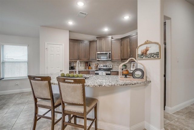 kitchen with visible vents, tasteful backsplash, light stone counters, a peninsula, and stainless steel appliances