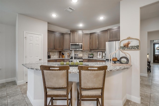 kitchen featuring visible vents, decorative backsplash, appliances with stainless steel finishes, and a kitchen breakfast bar