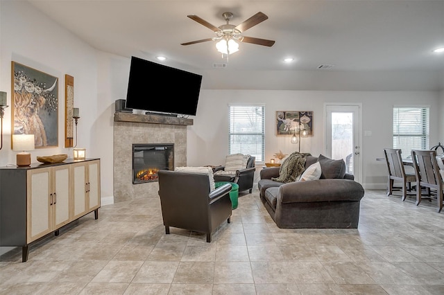 living area with a ceiling fan, visible vents, a tiled fireplace, and plenty of natural light