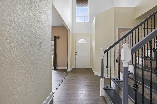 entryway with baseboards, dark wood finished floors, a textured wall, a towering ceiling, and stairs