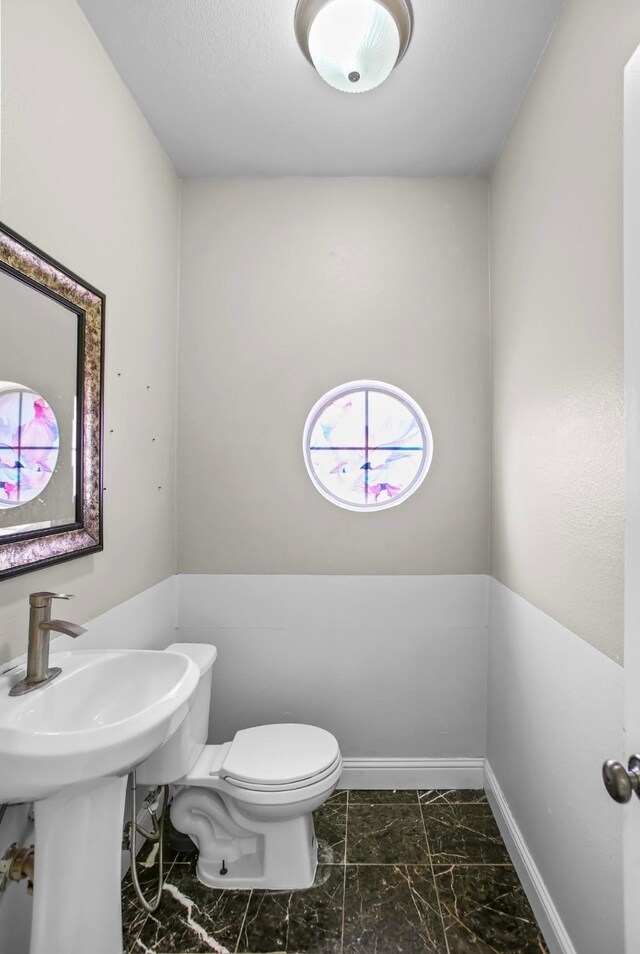 bathroom with marble finish floor, toilet, and baseboards