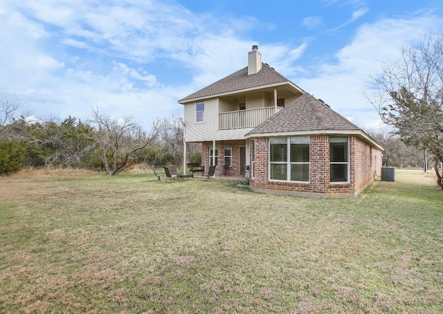 rear view of property featuring a lawn, a balcony, a chimney, central air condition unit, and brick siding