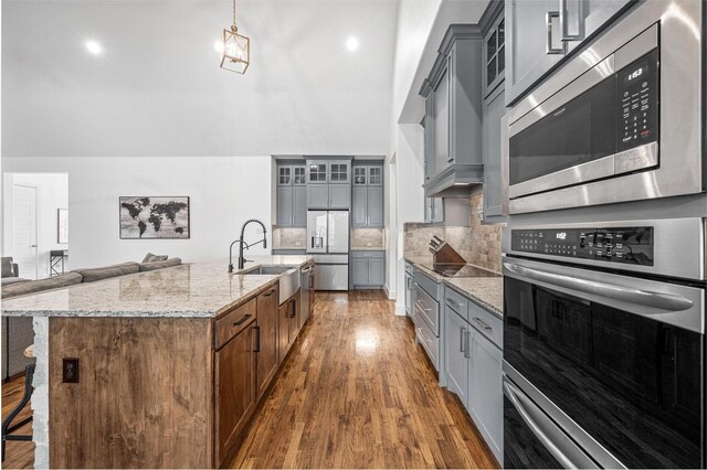 kitchen featuring appliances with stainless steel finishes, glass insert cabinets, light stone counters, and a sink