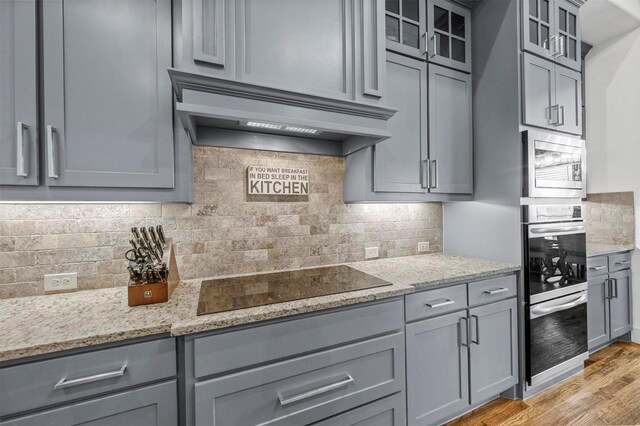 kitchen with light stone counters, premium range hood, glass insert cabinets, and black electric cooktop