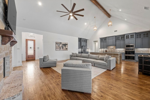 living room featuring visible vents, a fireplace with raised hearth, wood finished floors, beamed ceiling, and high vaulted ceiling