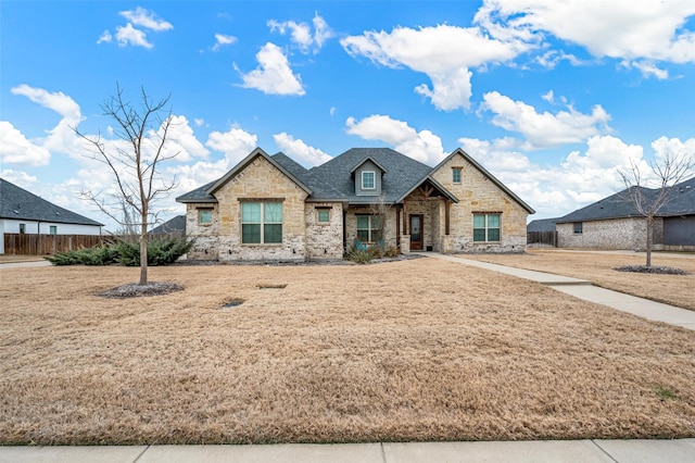 view of front of home featuring stone siding, fence, and a front lawn