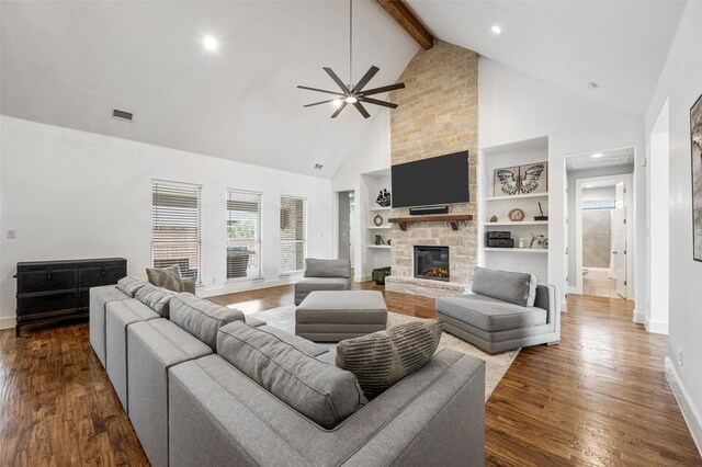 living area with baseboards, visible vents, dark wood-style floors, beamed ceiling, and a stone fireplace