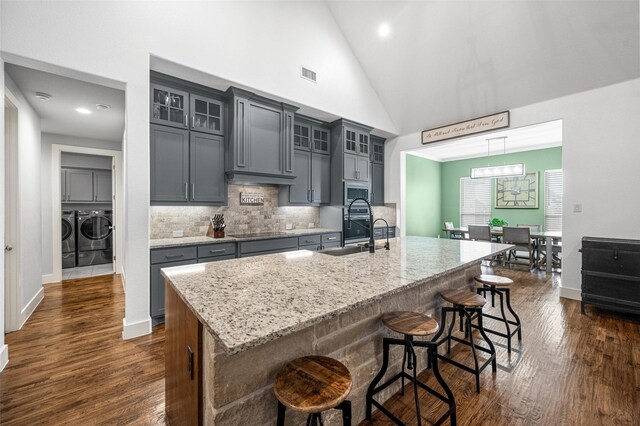 kitchen featuring an island with sink, glass insert cabinets, black electric cooktop, separate washer and dryer, and a sink