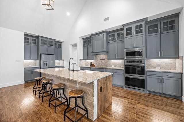 kitchen featuring light stone counters, a kitchen breakfast bar, a kitchen island with sink, stainless steel appliances, and a sink