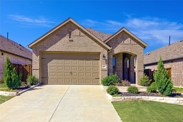 french country inspired facade featuring brick siding, roof with shingles, concrete driveway, an attached garage, and fence