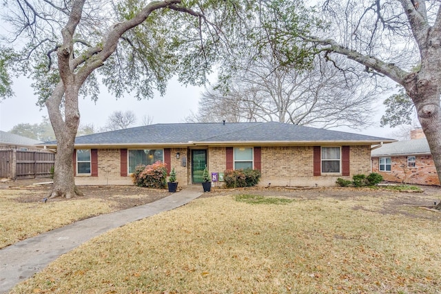 ranch-style home with brick siding, a shingled roof, fence, and a front yard