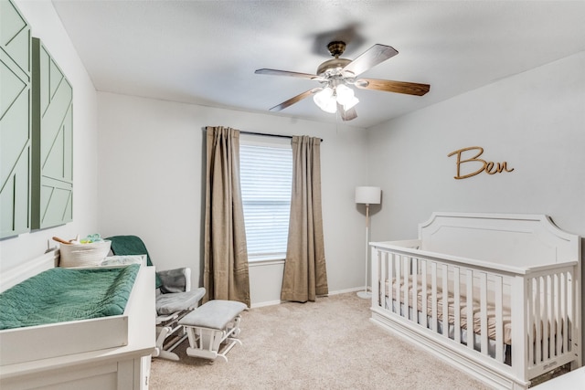 bedroom with light colored carpet, ceiling fan, a crib, and baseboards