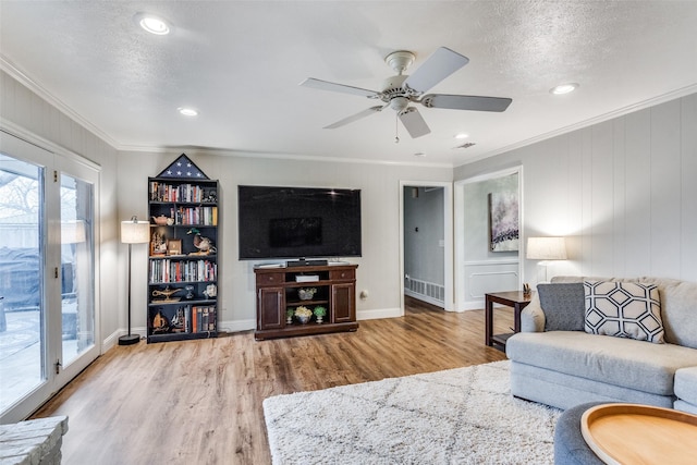 living room with a textured ceiling, ceiling fan, baseboards, ornamental molding, and light wood-type flooring