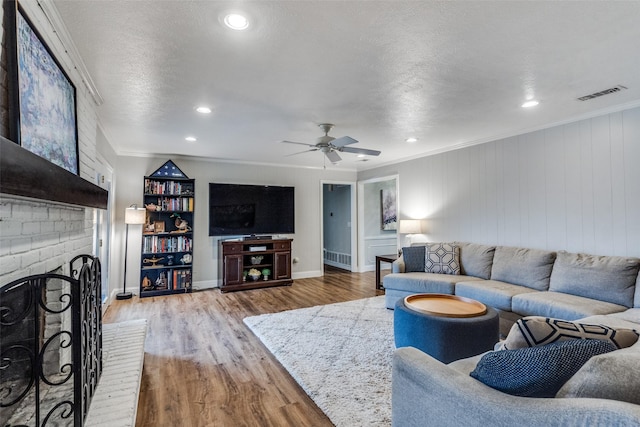 living room featuring a brick fireplace, visible vents, wood finished floors, and ornamental molding