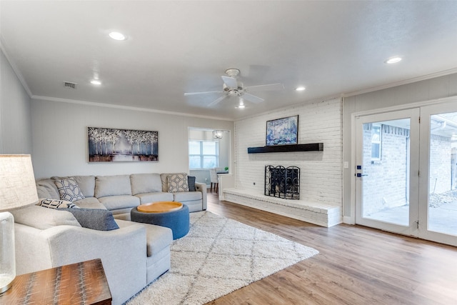 living room featuring crown molding, visible vents, a ceiling fan, a brick fireplace, and wood finished floors