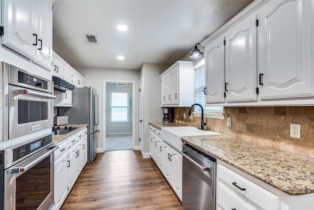 kitchen featuring under cabinet range hood, a sink, white cabinets, appliances with stainless steel finishes, and backsplash