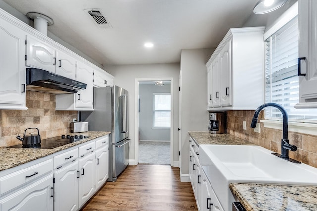 kitchen featuring visible vents, black electric stovetop, under cabinet range hood, white cabinetry, and a sink