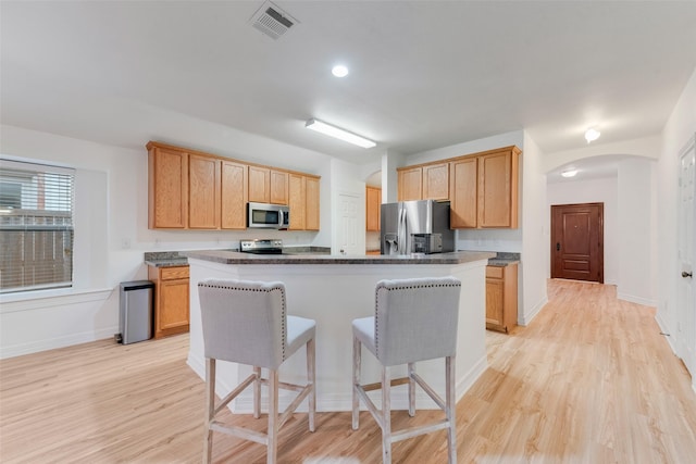 kitchen featuring arched walkways, stainless steel appliances, dark countertops, and a kitchen island