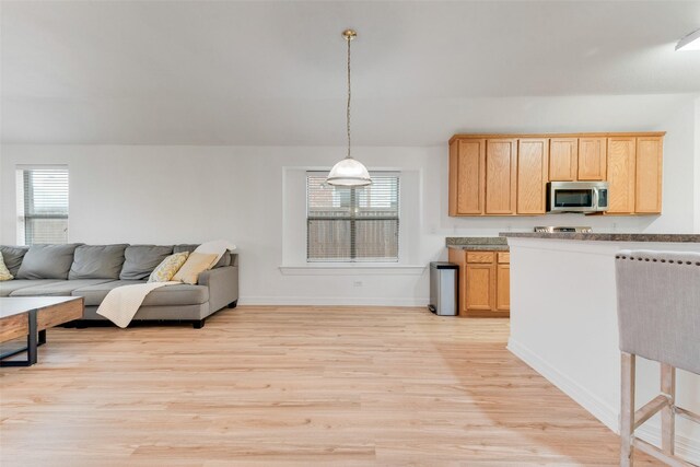 kitchen with pendant lighting, light wood finished floors, stainless steel microwave, light brown cabinetry, and open floor plan