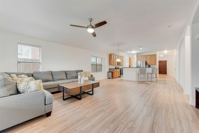 living area featuring light wood-style floors, plenty of natural light, arched walkways, and ceiling fan