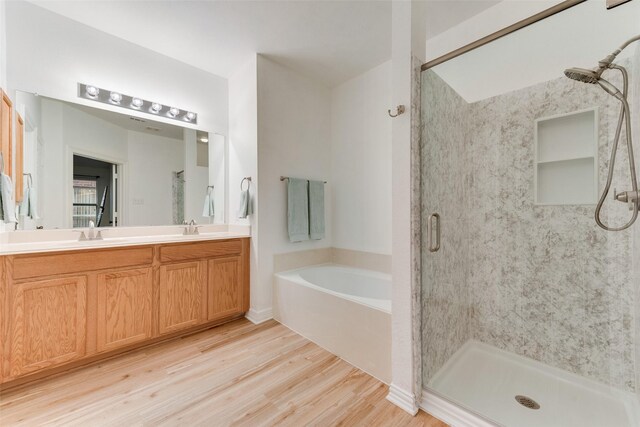 bathroom featuring double vanity, wood finished floors, a sink, and a bath